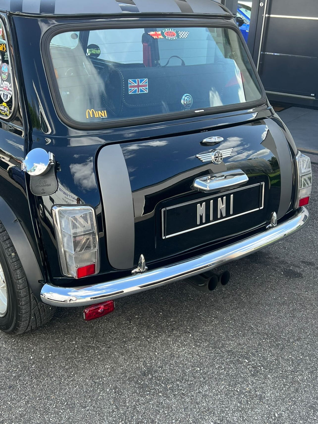 Vue arrière d'une Mini Austin noire équipée du kit adhésif Union Jack 2.0 dans ses cabochons de feux transparents

 Copier