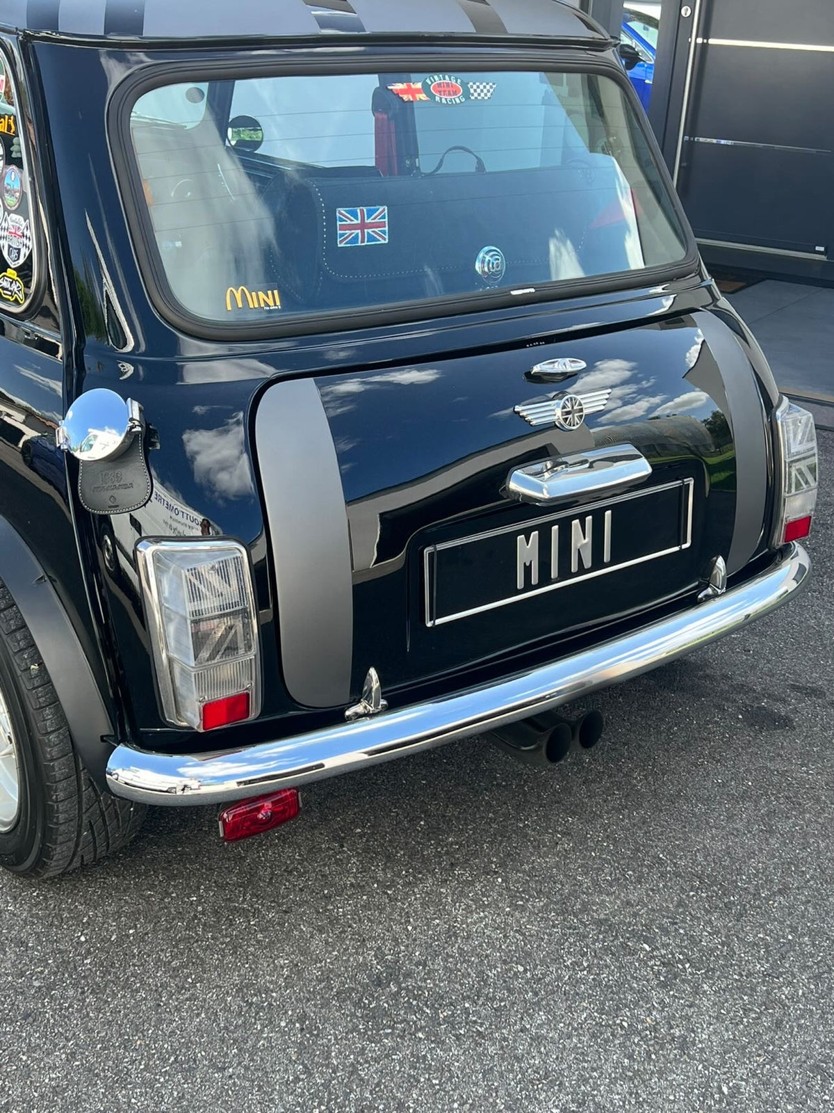 Vue arrière d'une Mini Austin noire équipée du kit adhésif Union Jack 2.0 dans ses cabochons de feux transparents

 Copier